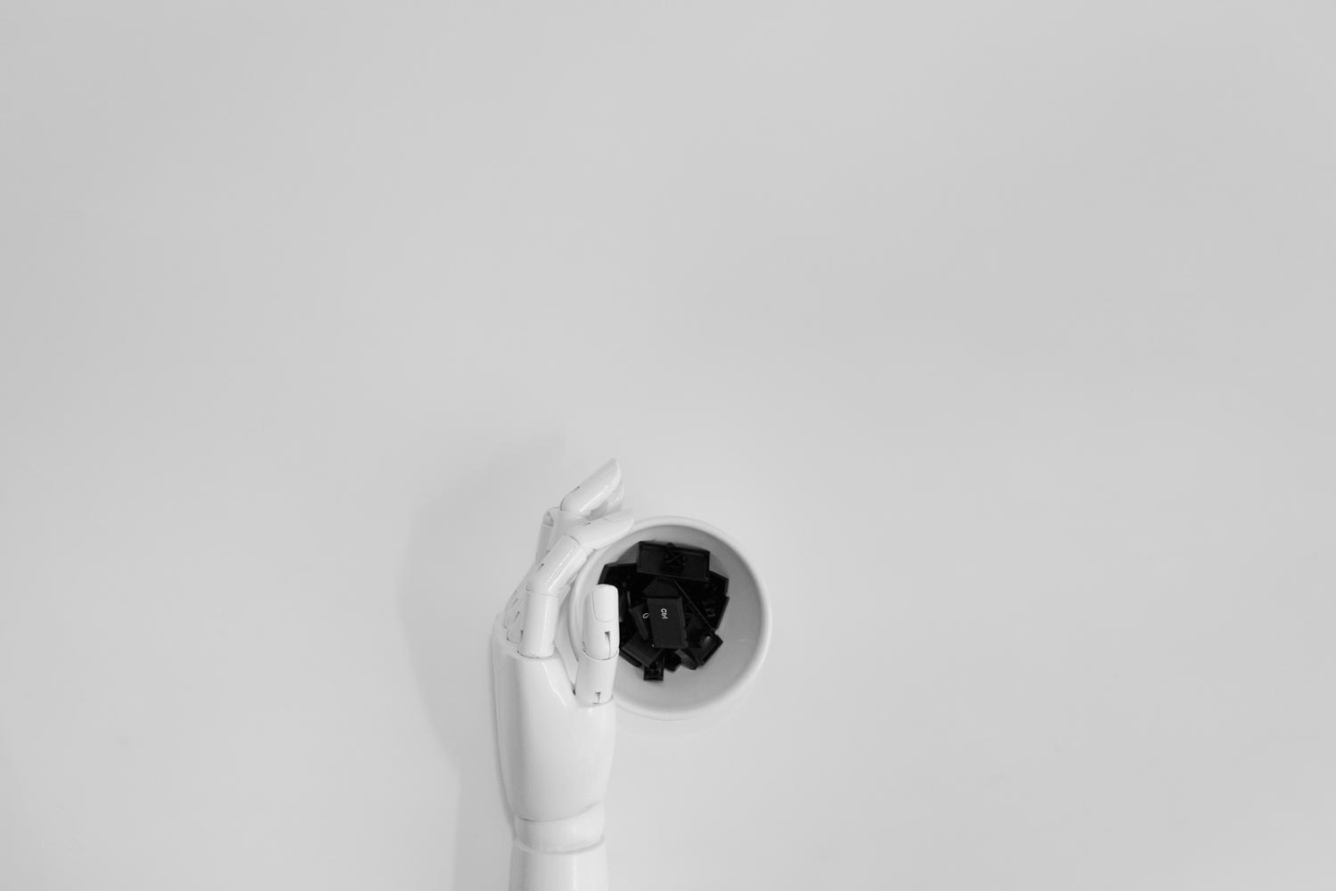 Mano robótica blanca sosteniendo teclas de teclado negras, simbolizando la automatización y la IA en el trabajo de oficina. Mano robótica blanca sosteniendo teclas de teclado negras, simbolizando la automatización y la IA en el trabajo de oficina.