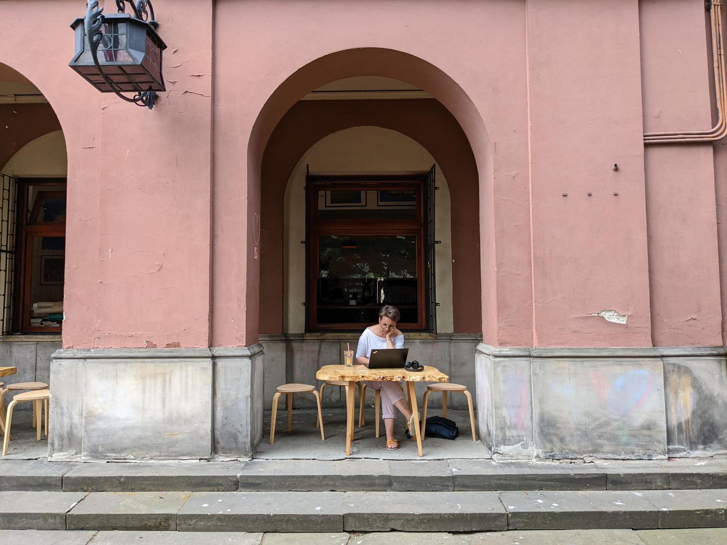 Mujer trabajando con un portátil en la terraza de una cafetería, ejemplificando el perfil de nómada digital. Mujer trabajando con un portátil en la terraza de una cafetería, ejemplificando el perfil de nómada digital.