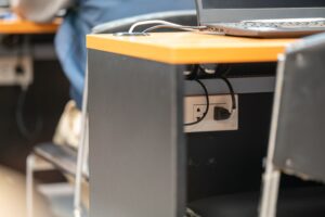 Portátil conectado a la corriente eléctrica en un escritorio moderno de oficina, ilustrando el consumo energético de los ordenadores portátiles y el consumo fantasma cuando permanecen enchufados