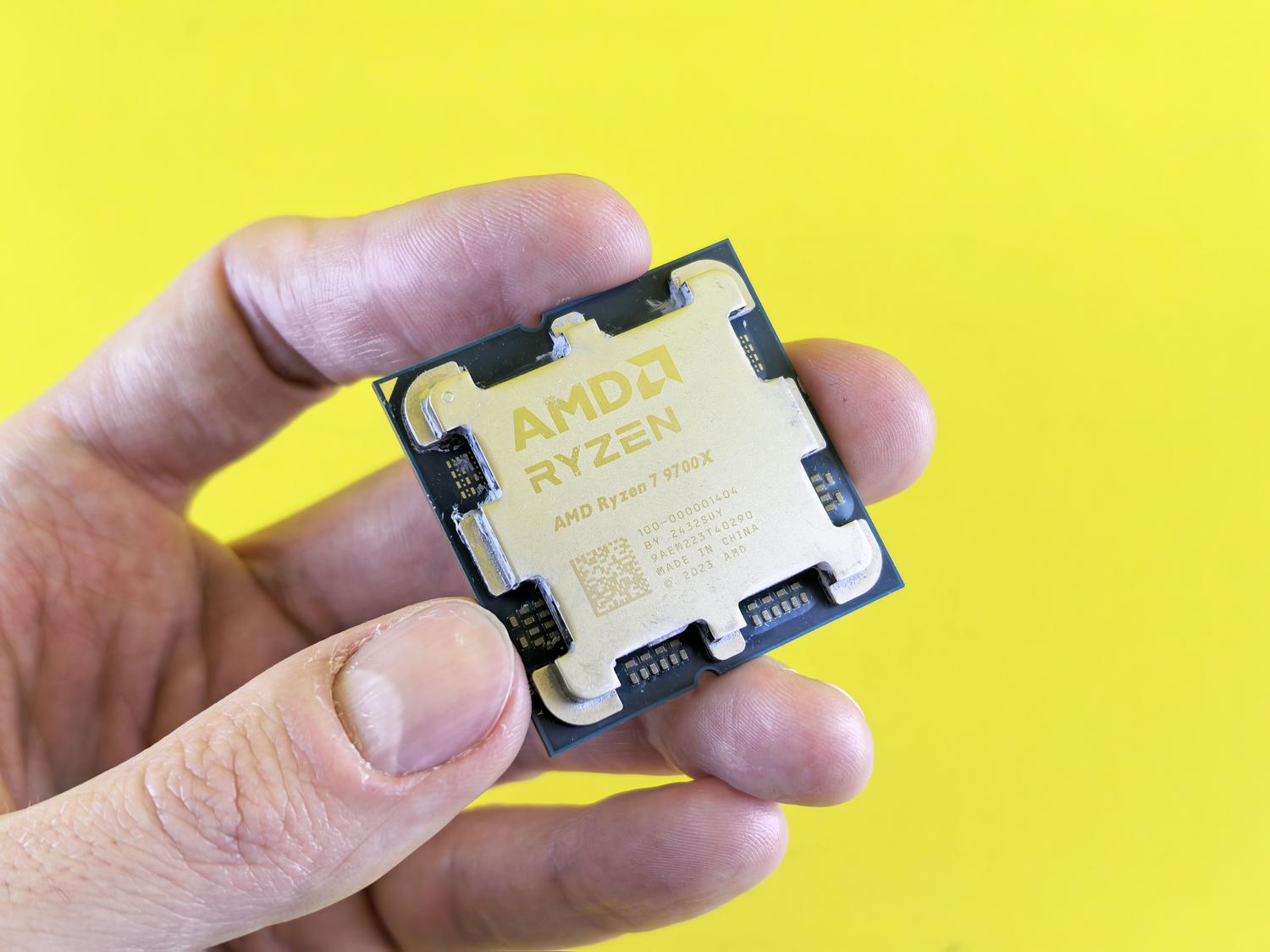 Primer plano de un procesador AMD Ryzen 7 9700X sostenido en la mano, destacando su diseño moderno y el IHS dorado. Primer plano de un procesador AMD Ryzen 7 9700X sostenido en la mano, destacando su diseño moderno y el IHS dorado.