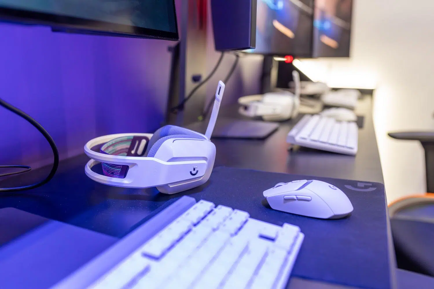 Primer plano de un setup gaming profesional con auriculares inalámbricos blancos, ratón y teclado mecánico bajo una iluminación RGB púrpura y azul. Primer plano de un setup gaming profesional con auriculares inalámbricos blancos, ratón y teclado mecánico bajo una iluminación RGB púrpura y azul.