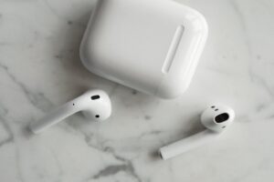 Auriculares inalámbricos blancos tipo earbuds con su estuche de carga sobre una superficie de mármol, mostrando el diseño minimalista y moderno de los dispositivos de audio.