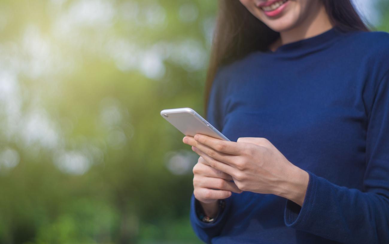 Mujer sonriente usando un smartphone al aire libre, transmitiendo la sensación de libertad y conectividad que prometen los planes de datos ilimitados