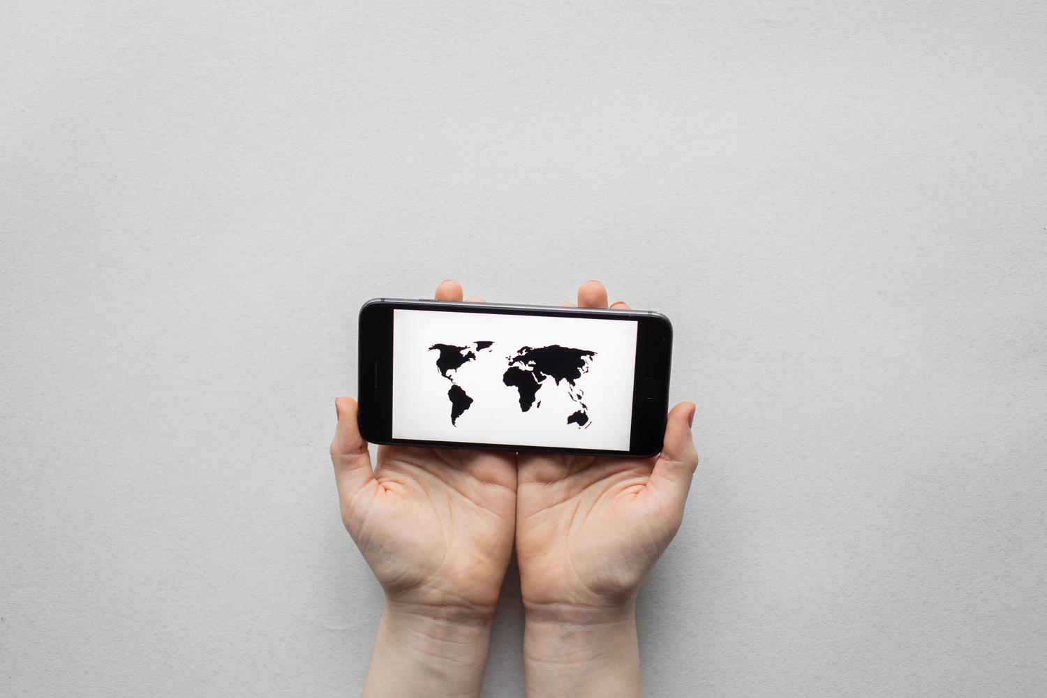 Manos sosteniendo un teléfono móvil que muestra un mapa mundial, ilustrando el concepto de geolocalización basada en IP a nivel global. Manos sosteniendo un teléfono móvil que muestra un mapa mundial, ilustrando el concepto de geolocalización basada en IP a nivel global.