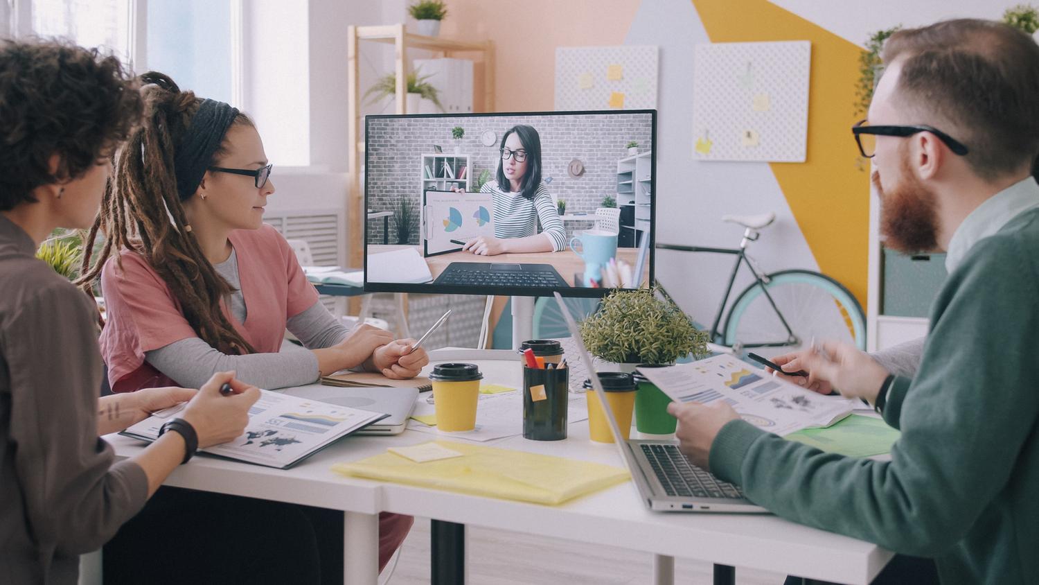 Equipo profesional en una reunión híbrida combinando presencia física y videollamada en una oficina contemporánea y luminosa. Equipo profesional en una reunión híbrida combinando presencia física y videollamada en una oficina contemporánea y luminosa.