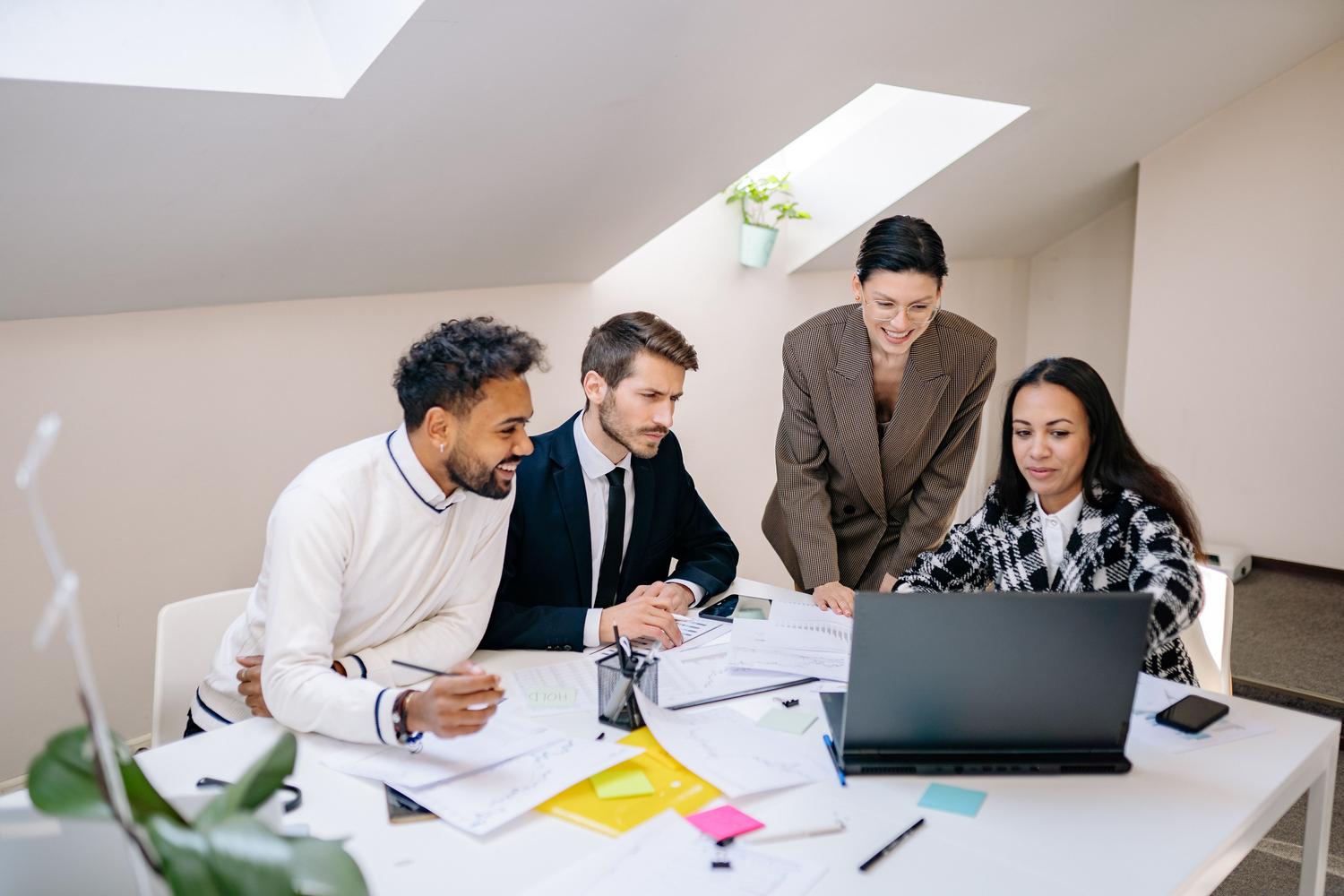 Equipo de trabajo diverso analizando documentos y utilizando un portátil en una mesa de reuniones en una oficina iluminada. Equipo de trabajo diverso analizando documentos y utilizando un portátil en una mesa de reuniones en una oficina iluminada.