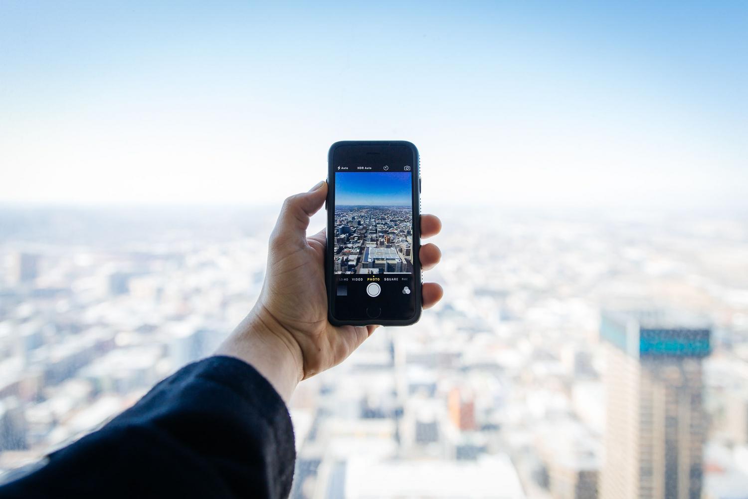 Persona utilizando un smartphone para capturar la vista de una ciudad, simbolizando la interacción digital del ciudadano y la administración electrónica. Persona utilizando un smartphone para capturar la vista de una ciudad, simbolizando la interacción digital del ciudadano y la administración electrónica.