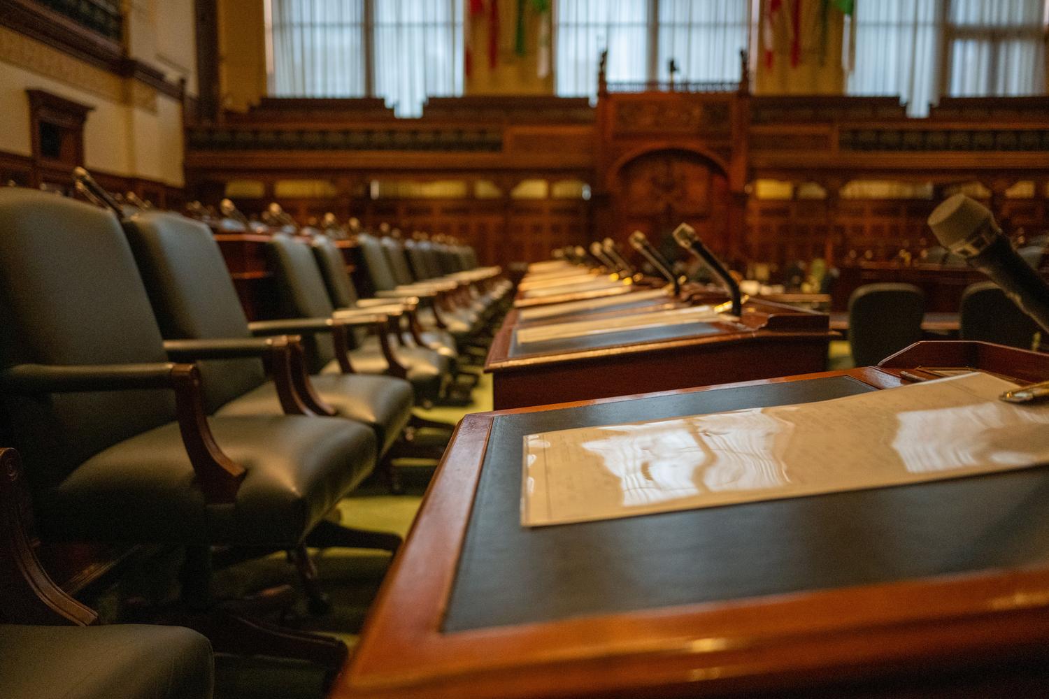 Vista interior de una cámara legislativa vacía con micrófonos y documentos, simbolizando el marco normativo, el liderazgo institucional y la toma de decisiones en la gobernanza. Vista interior de una cámara legislativa vacía con micrófonos y documentos, simbolizando el marco normativo, el liderazgo institucional y la toma de decisiones en la gobernanza.