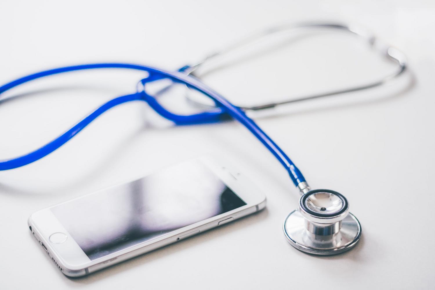 Smartphone y estetoscopio sobre una superficie blanca, representando la gestión de la salud digital. Smartphone y estetoscopio sobre una superficie blanca, representando la gestión de la salud digital.