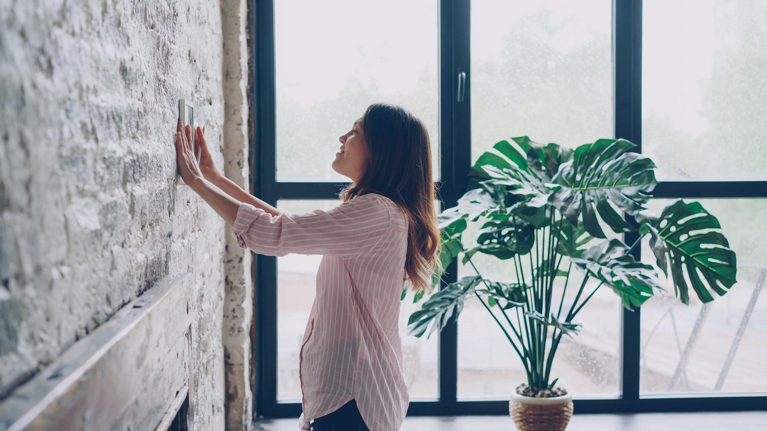 Mujer ajustando un termostato inteligente en un hogar moderno, representando la optimización energética y la inteligencia ambiental. Mujer ajustando un termostato inteligente en un hogar moderno, representando la optimización energética y la inteligencia ambiental.