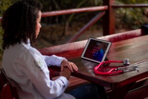 Profesional sanitaria utilizando una tablet y un estetoscopio en un entorno exterior, representando la movilidad y el acceso a la salud digital en espacios públicos.