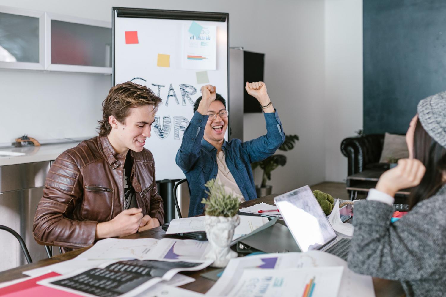 Grupo de emprendedores celebrando un éxito en su oficina con un whiteboard de 'Start Up', simbolizando los exits y el crecimiento sostenible. Grupo de emprendedores celebrando un éxito en su oficina con un whiteboard de 'Start Up', simbolizando los exits y el crecimiento sostenible.
