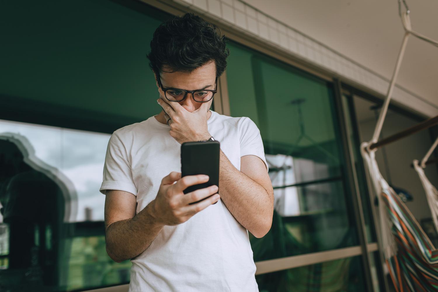 Recuperar cuenta de WhatsApp - pérdida de acceso Hombre preocupado mirando la pantalla de su smartphone, representando la sensación de perder el acceso a una cuenta.