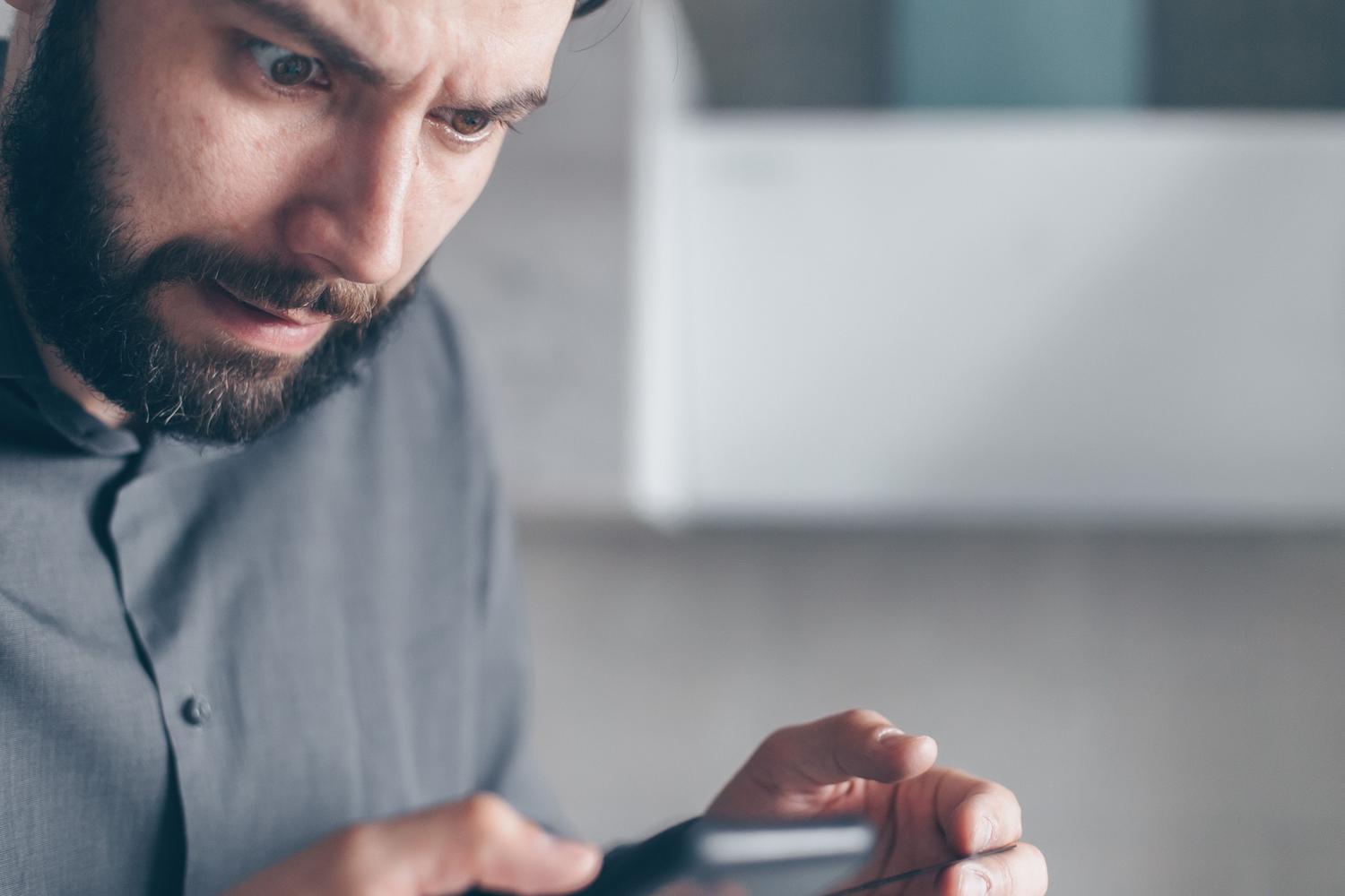 Cuenta suspendida o hackeada de WhatsApp Hombre con expresión de sorpresa y frustración al usar su móvil, ideal para secciones sobre cuentas suspendidas o hackeo.
