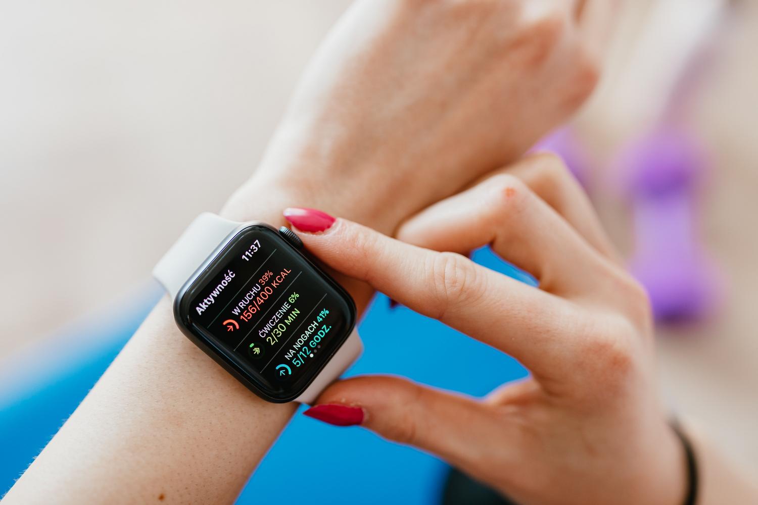 Mujer revisando sus anillos de actividad y estadísticas de salud en su smartwatch mientras descansa sobre una esterilla de yoga. Mujer revisando sus anillos de actividad y estadísticas de salud en su smartwatch mientras descansa sobre una esterilla de yoga.