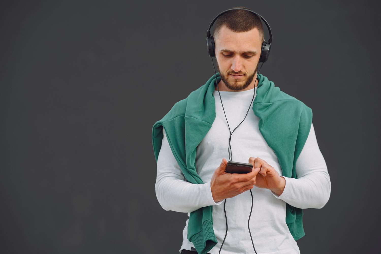 Hombre joven utilizando auriculares y móvil para gestionar su música Hombre joven utilizando auriculares y móvil para gestionar su música