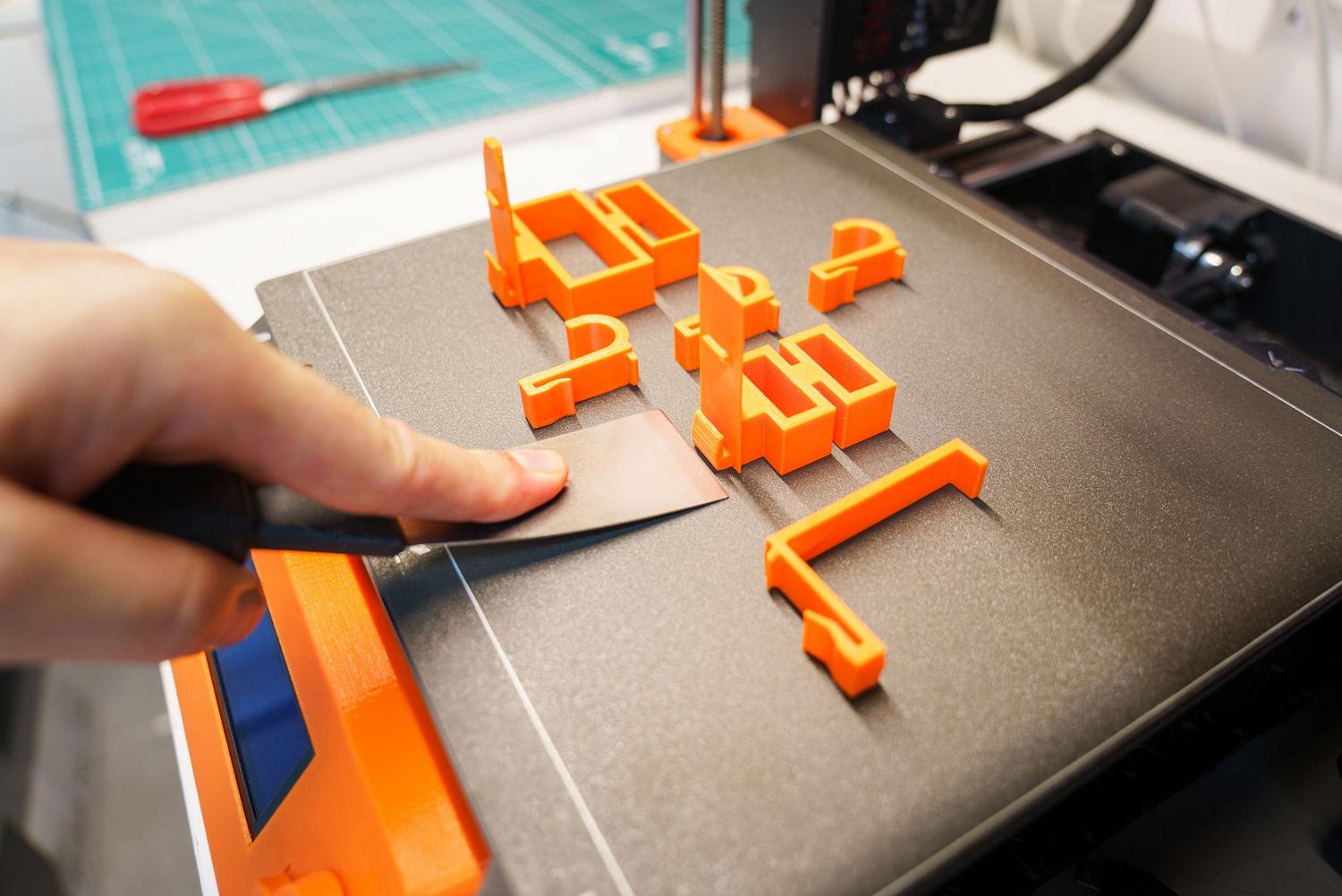Uso de una espátula para retirar una pieza impresa en 3D de la cama de impresión. Uso de una espátula para retirar una pieza impresa en 3D de la cama de impresión.