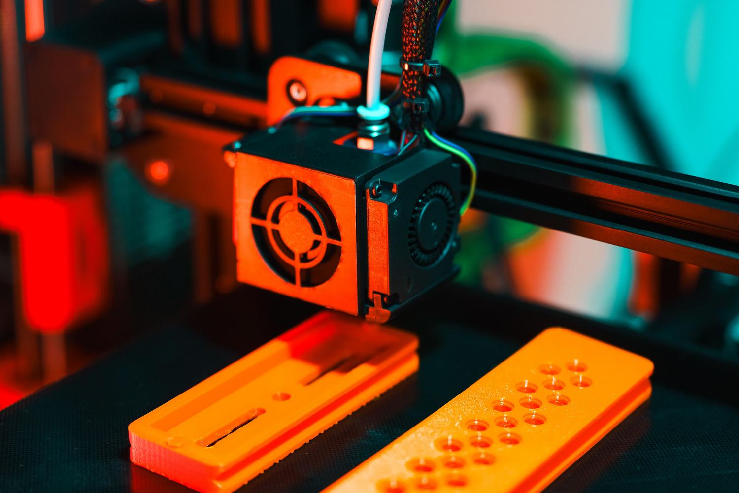 Proceso de impresión 3D FDM extruyendo filamento plástico de color naranja. Proceso de impresión 3D FDM extruyendo filamento plástico de color naranja.