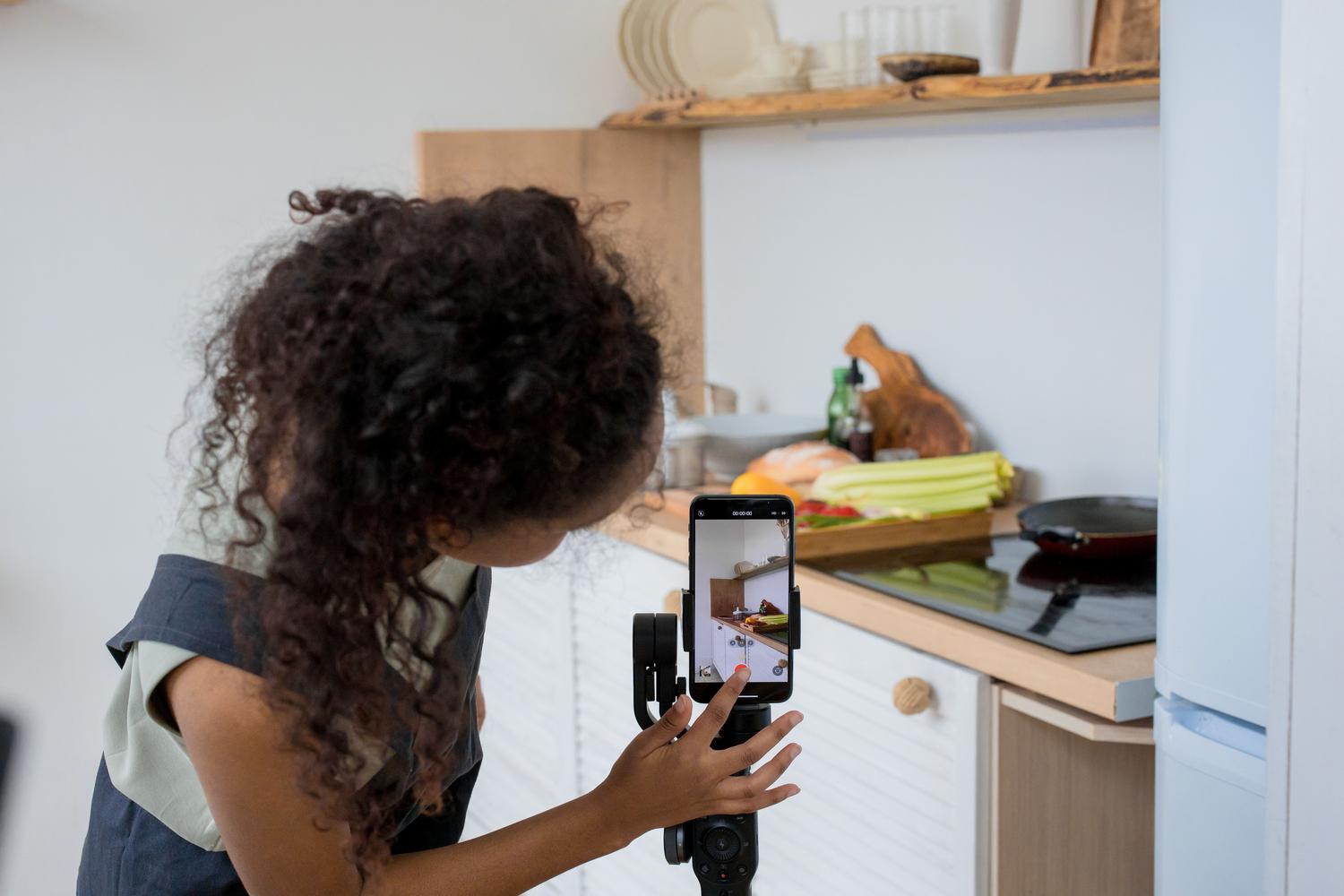 Mujer grabando un tutorial de cocina con un estabilizador de móvil, ejemplificando la creación de contenido viral y creativo. Mujer grabando un tutorial de cocina con un estabilizador de móvil, ejemplificando la creación de contenido viral y creativo.