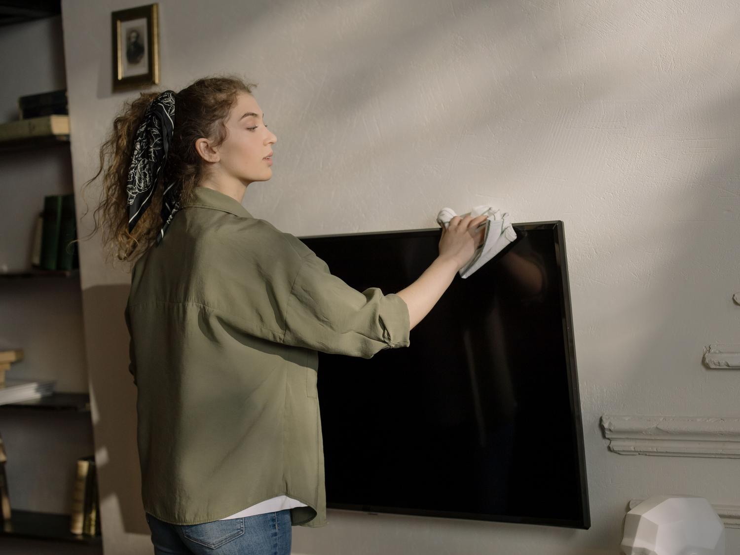 Una persona limpiando cuidadosamente la pantalla de un televisor plano en un ambiente hogareño. Una persona limpiando cuidadosamente la pantalla de un televisor plano en un ambiente hogareño.