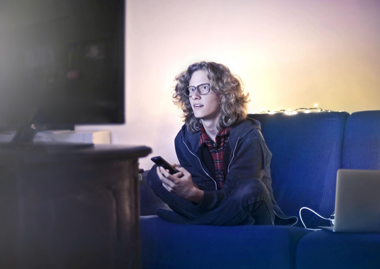 Persona ajustando la configuración de la aplicación de Netflix en su móvil mientras ve la televisión Persona ajustando la configuración de la aplicación de Netflix en su móvil mientras ve la televisión