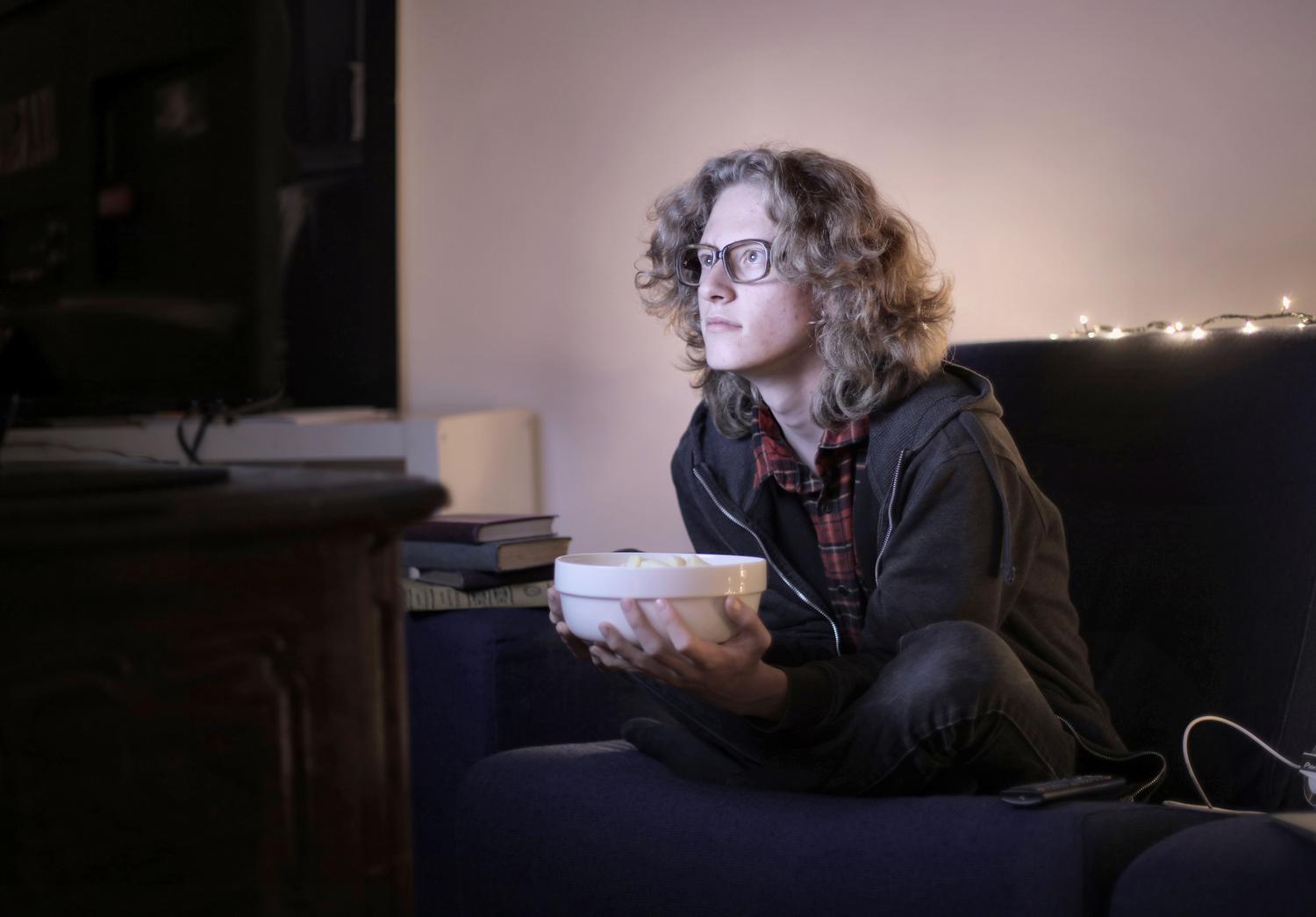 Joven disfrutando de un maratón de series con palomitas en un ambiente acogedor, ilustrando el binge-watching Joven disfrutando de un maratón de series con palomitas en un ambiente acogedor, ilustrando el binge-watching
