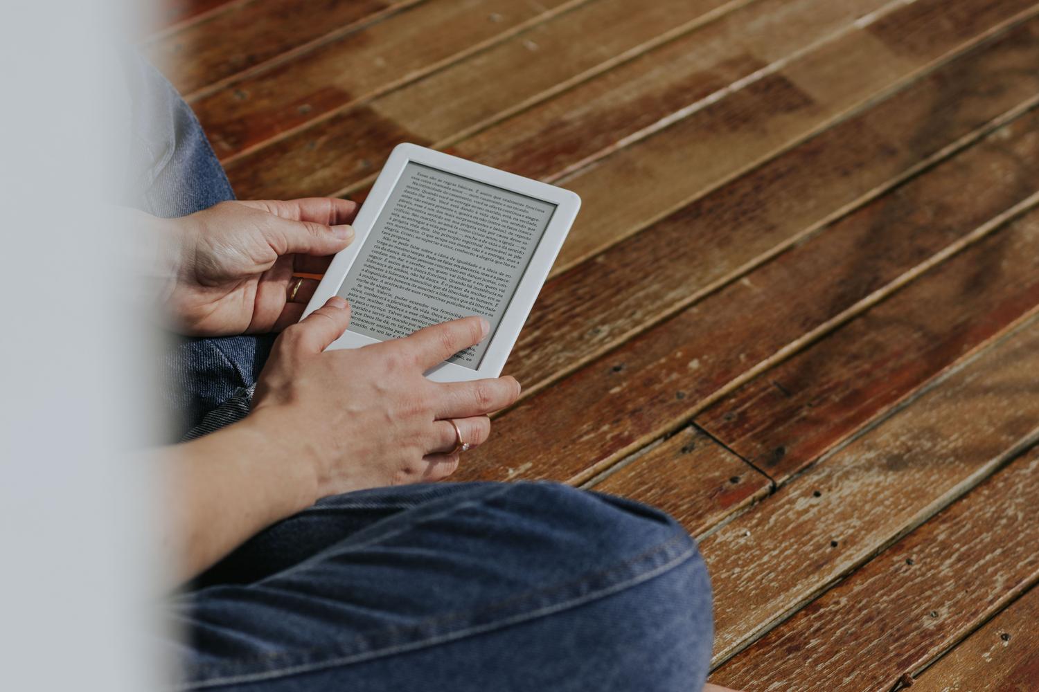 Manos sosteniendo un lector de libros electrónicos (e-reader) en un ambiente acogedor, ideal para representar la configuración de dispositivos Kindle. Manos sosteniendo un lector de libros electrónicos (e-reader) en un ambiente acogedor, ideal para representar la configuración de dispositivos Kindle.