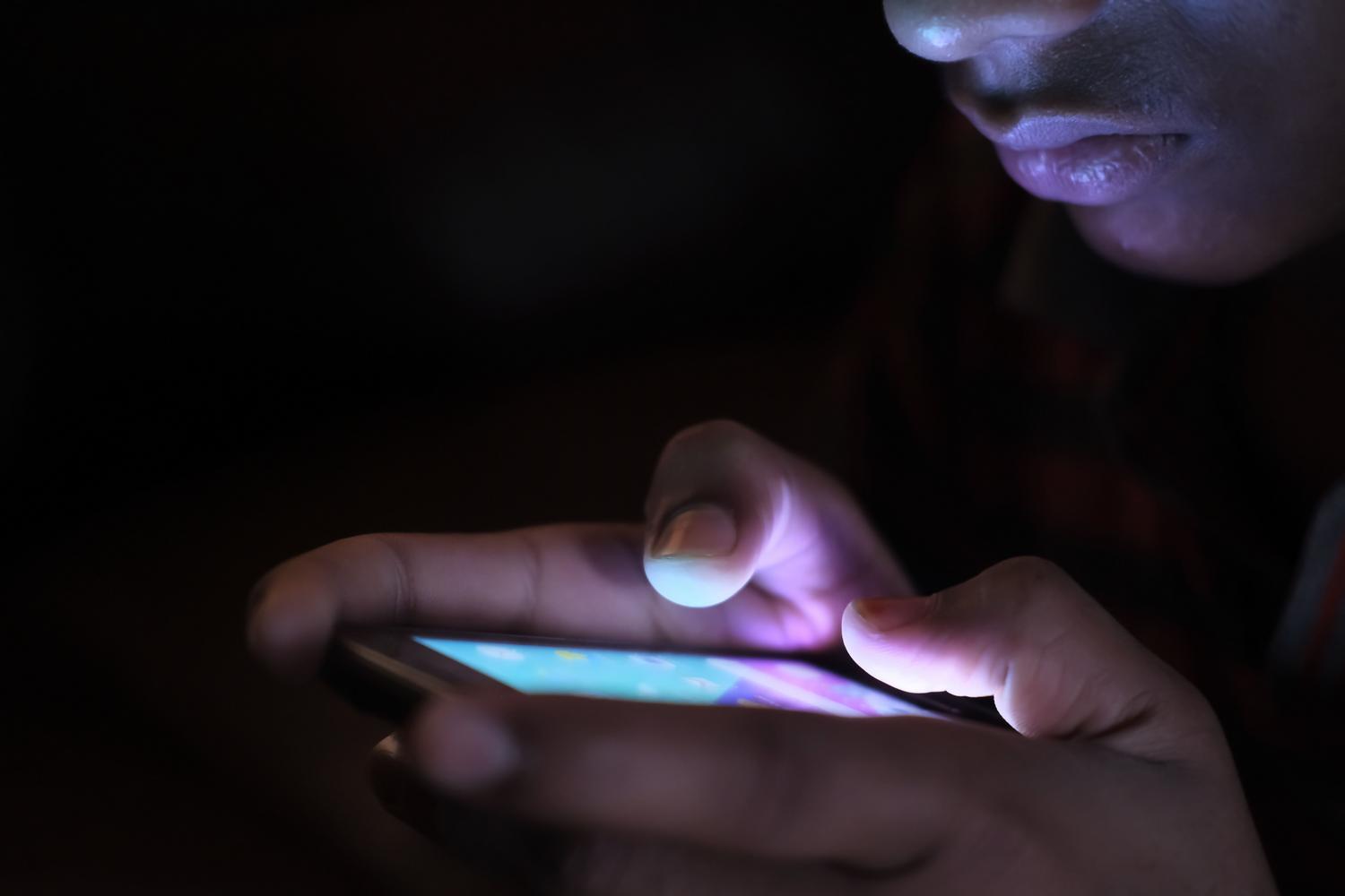 Smartphone iluminando el rostro de una persona en la oscuridad, representando la pantalla de bloqueo encendida. Smartphone iluminando el rostro de una persona en la oscuridad, representando la pantalla de bloqueo encendida.